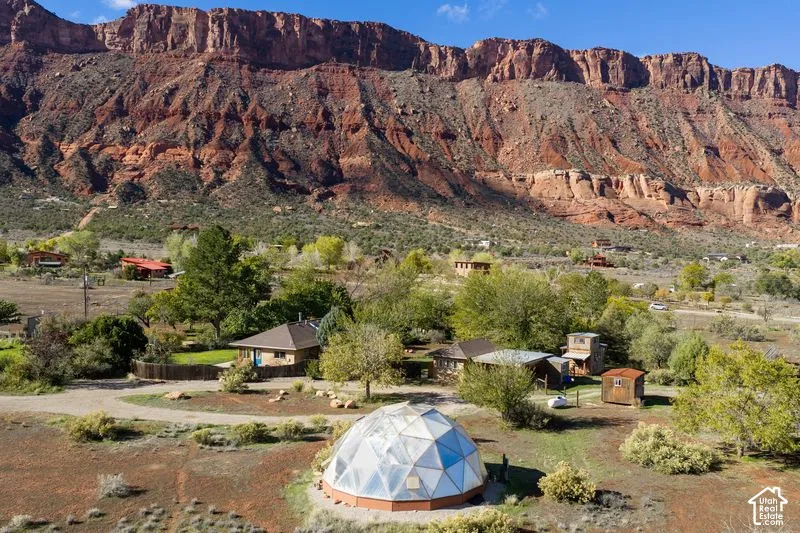 Geodesic dome structure situated on expansive acreage featuring native landscaping, mature trees, and a backdrop of prominent rock formations