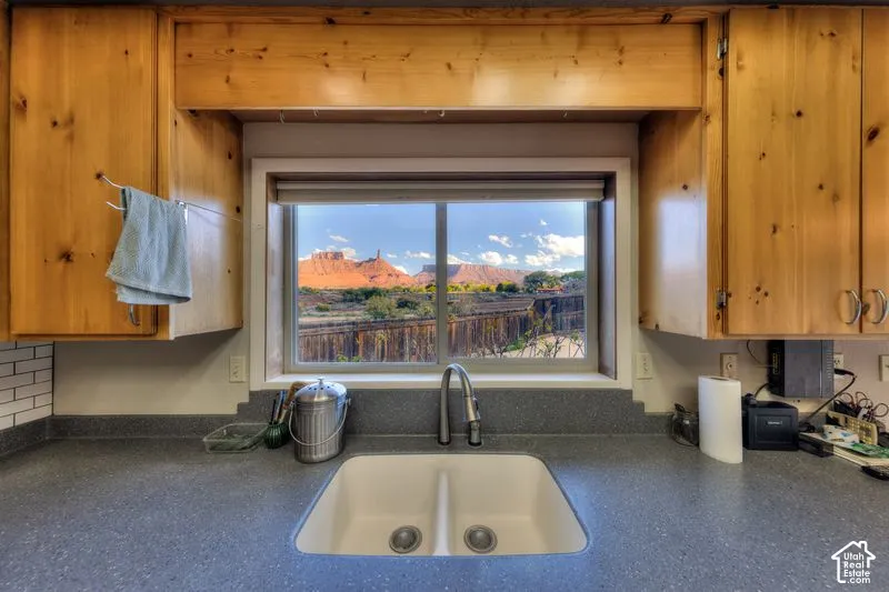 Kitchen sink area featuring solid surface countertops, a dual-basin white sink, high-arch pull-down faucet, custom knotty wood cabinetry, and a large window showcasing red rock canyon formations