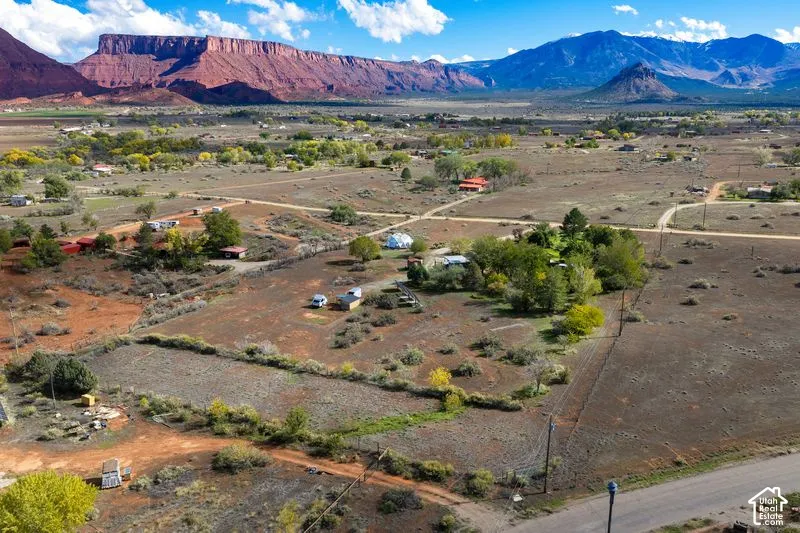 Expansive desert landscape featuring prominent red rock mountain backdrops, mature trees, and natural vegetation