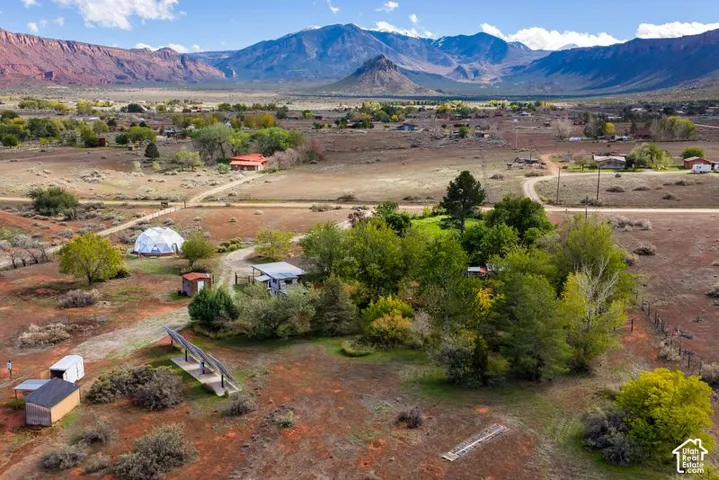Expansive desert acreage featuring mature trees, a geodesic dome structure, a solar panel array, and mountain range backdrop