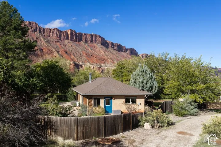 Single-story residence featuring tan exterior siding, a hipped roof, wood-slat privacy fencing, and a prominent mountain backdrop