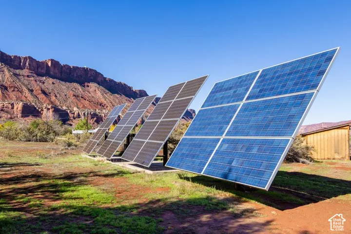 Ground-mounted solar panel array situated on natural desert landscape with rock formation backdrop