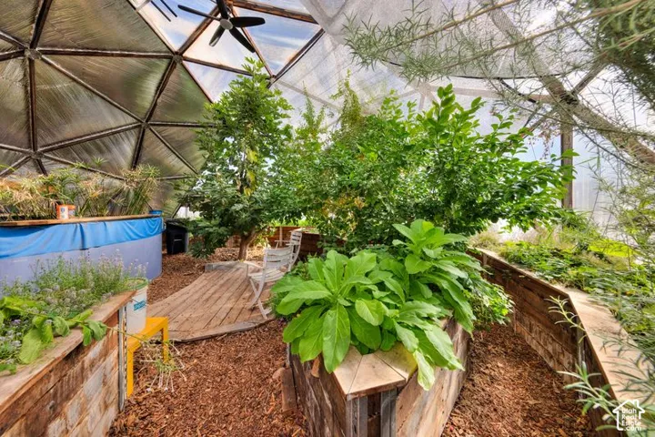 Geodesic dome greenhouse featuring a metal structural frame, integrated raised wooden planting beds, wood-chip ground covering, and an overhead ceiling fan