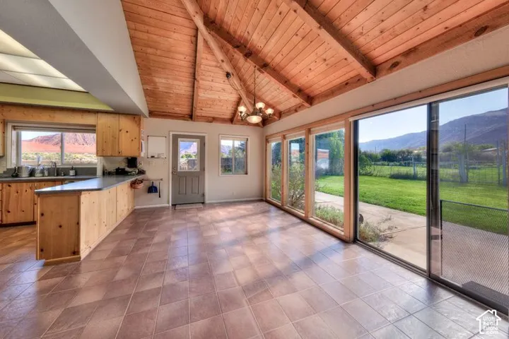 Vaulted natural wood ceiling with exposed beams, tile flooring, wraparound sliding glass doors, wooden cabinetry, and mountain backdrop