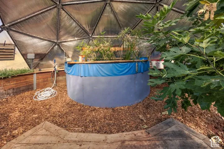 Geodesic greenhouse featuring a metal frame, mulch flooring, wood-paneled walls, and a large circular water containment system with Gold Fish.