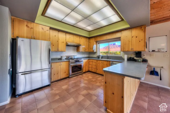 Kitchen featuring custom wood cabinetry, stainless steel appliances, tiled backsplash, and recessed coffered lighting, with a window framing a mountain backdrop