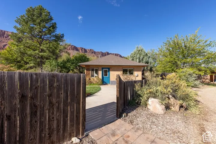Single-story residence featuring a stucco exterior, hipped roof, concrete walkway, enclosed wood fence, and mountain backdrop