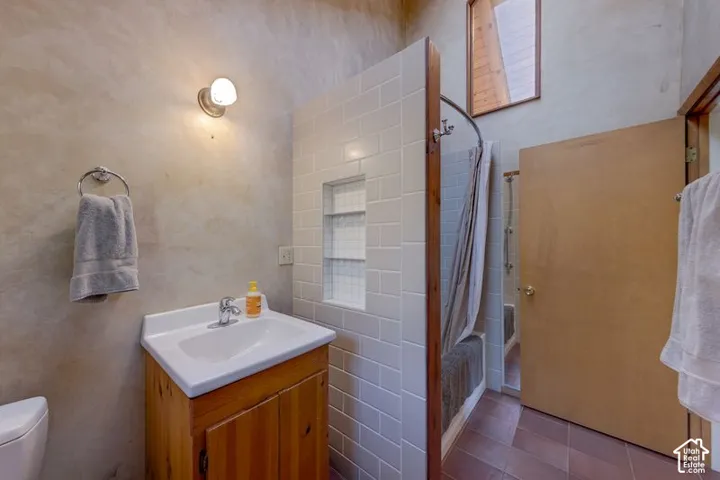 Bathroom featuring a wood vanity with a white basin, subway-tiled shower surround with integrated shelving, tile flooring, and high-reaching ceilings with a clerestory window