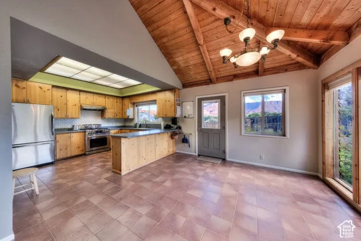 Kitchen featuring natural wood cabinetry, stainless steel appliances, tile flooring, and a vaulted ceiling with exposed wood beams and a multi-arm chandelier