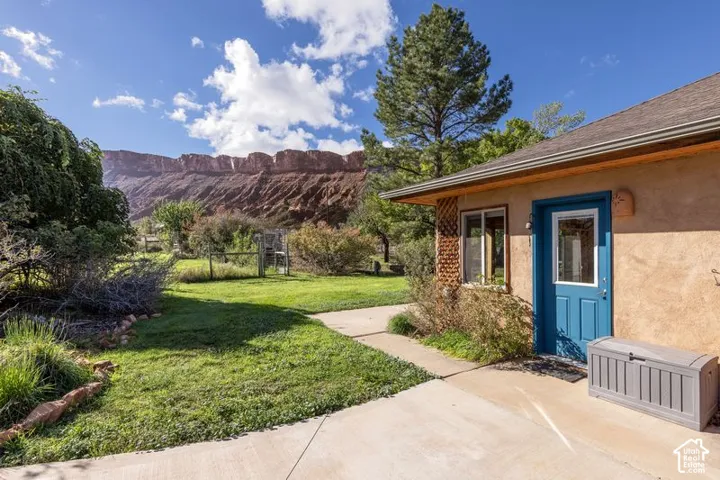 Exterior grounds featuring a concrete patio, grassy lawn, mature trees, and a desert mesa backdrop