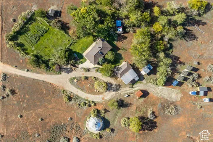 Aerial view of a sprawling property featuring multiple structures, a fenced garden area, mature trees, and solar panel arrays