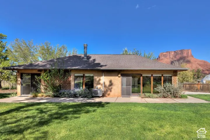 Exterior elevation featuring stucco siding, integrated lattice screening, concrete patio, and a backdrop of prominent rock formations