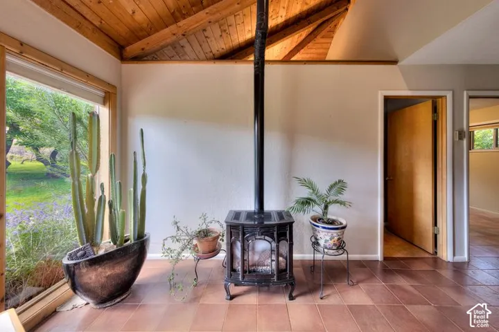 Vaulted ceiling with exposed wood-finish beams, freestanding cast-iron stove, large window, and tile flooring