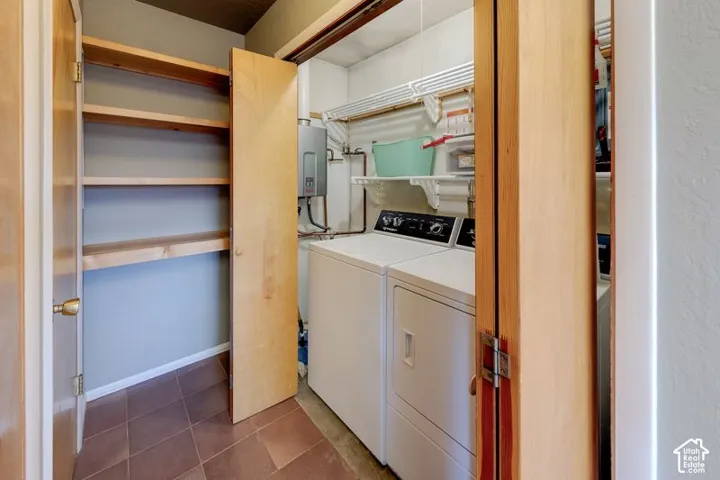 Utility space featuring built-in wood shelving, wall-mounted tankless water heater, and tile flooring