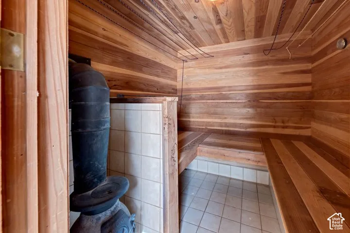 Sauna room featuring tongue-and-groove cedar paneling, tiered wood-plank seating, a tile-surround heater enclosure, and a cast-iron stove