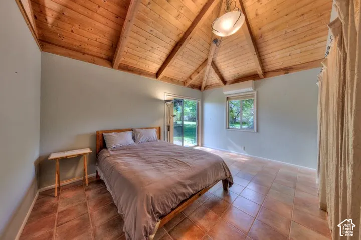 Vaulted ceiling with exposed wood beams, wood-plank ceiling finish, tile flooring, wall-mounted ductless climate control unit, and glass sliding door