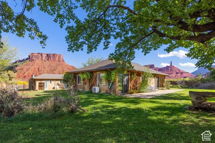 Single-story residence featuring wood-clad siding, a concrete patio, mature shade trees, and expansive red rock mountain scenery