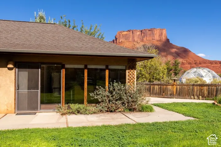 Exterior featuring concrete patio, floor-to-ceiling glass wall, wood-frame sliding door, latticework detailing, and red rock mesa backdrop