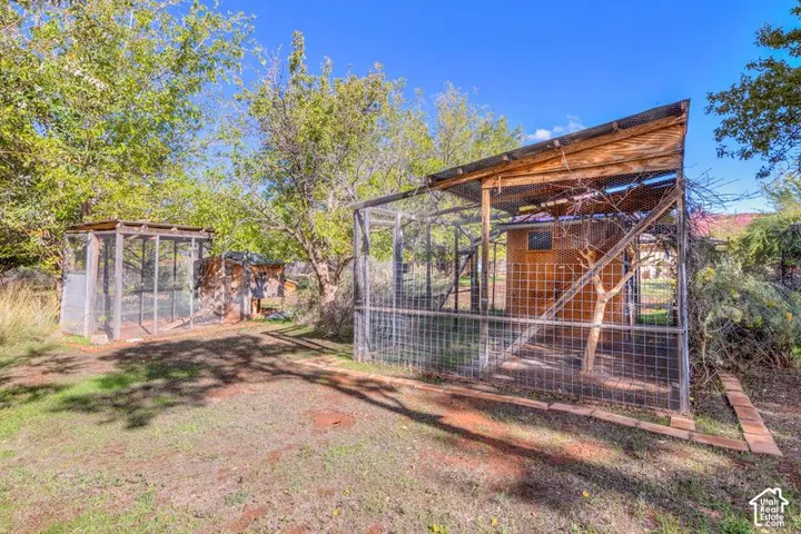 Outdoor area featuring two wood-frame structures with wire mesh enclosures, corrugated metal roofing, and surrounding mature trees