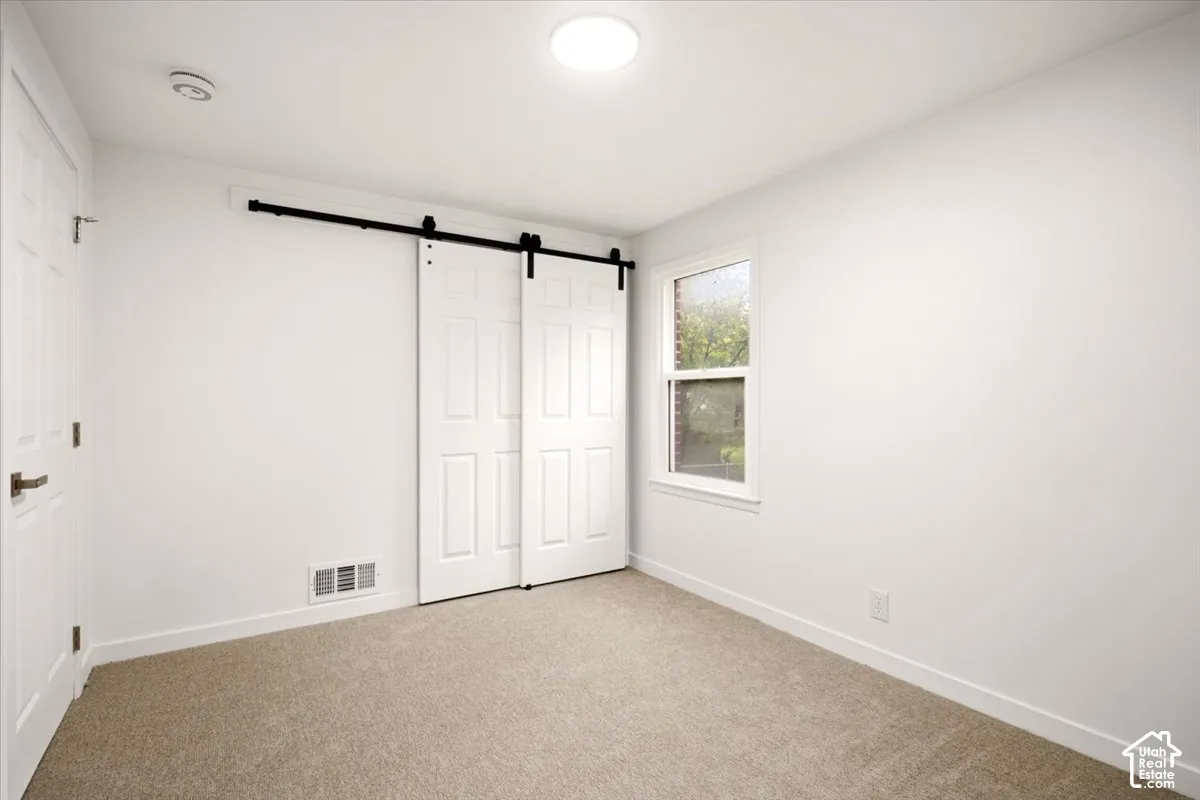 Room featuring wall-to-wall carpeting, dual white panel sliding barn doors with matte black hardware, and a single-hung window