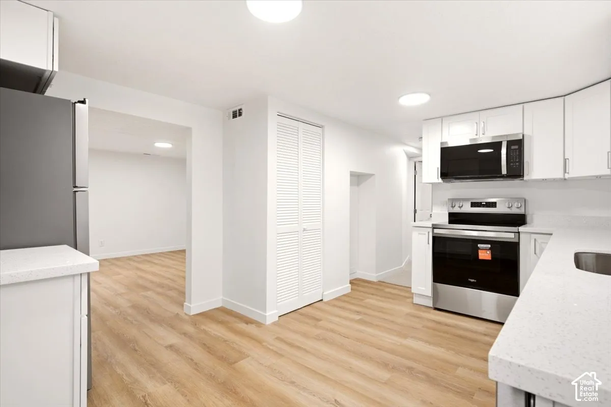 Kitchen featuring white shaker-style cabinetry, light-toned countertop surfaces, stainless steel appliances, and wood-finish flooring