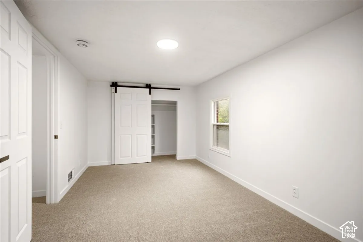 Room featuring wall-to-wall carpeting, single-pane window, white paneled doors, and a sliding barn-style door opening to a closet with built-in shelving