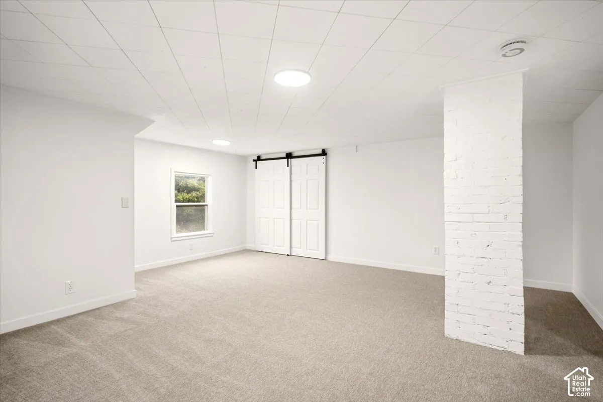 Open interior space featuring white painted brick architectural column, sliding barn-style doors, neutral carpeting, and recessed ceiling lighting