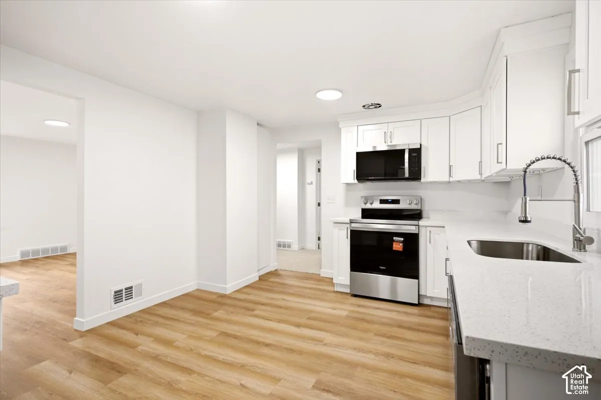 Kitchen featuring white shaker-style cabinetry, solid-surface countertops, stainless steel appliances, a pull-down kitchen faucet, and wood-finish flooring