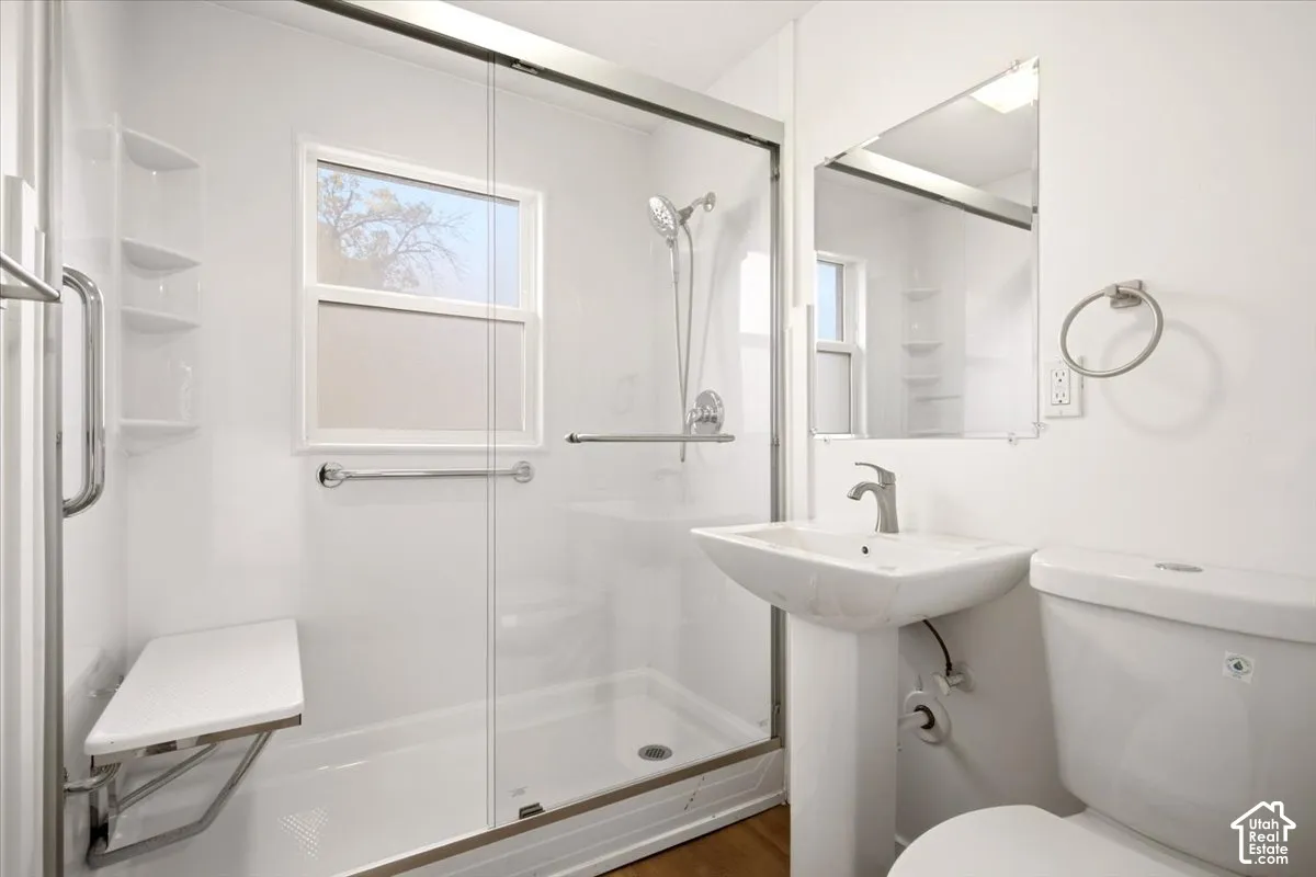 Walk-in shower enclosure with glass sliding doors, integrated bench seat, and handheld shower fixture, accompanied by a white pedestal sink and wall-mounted mirror