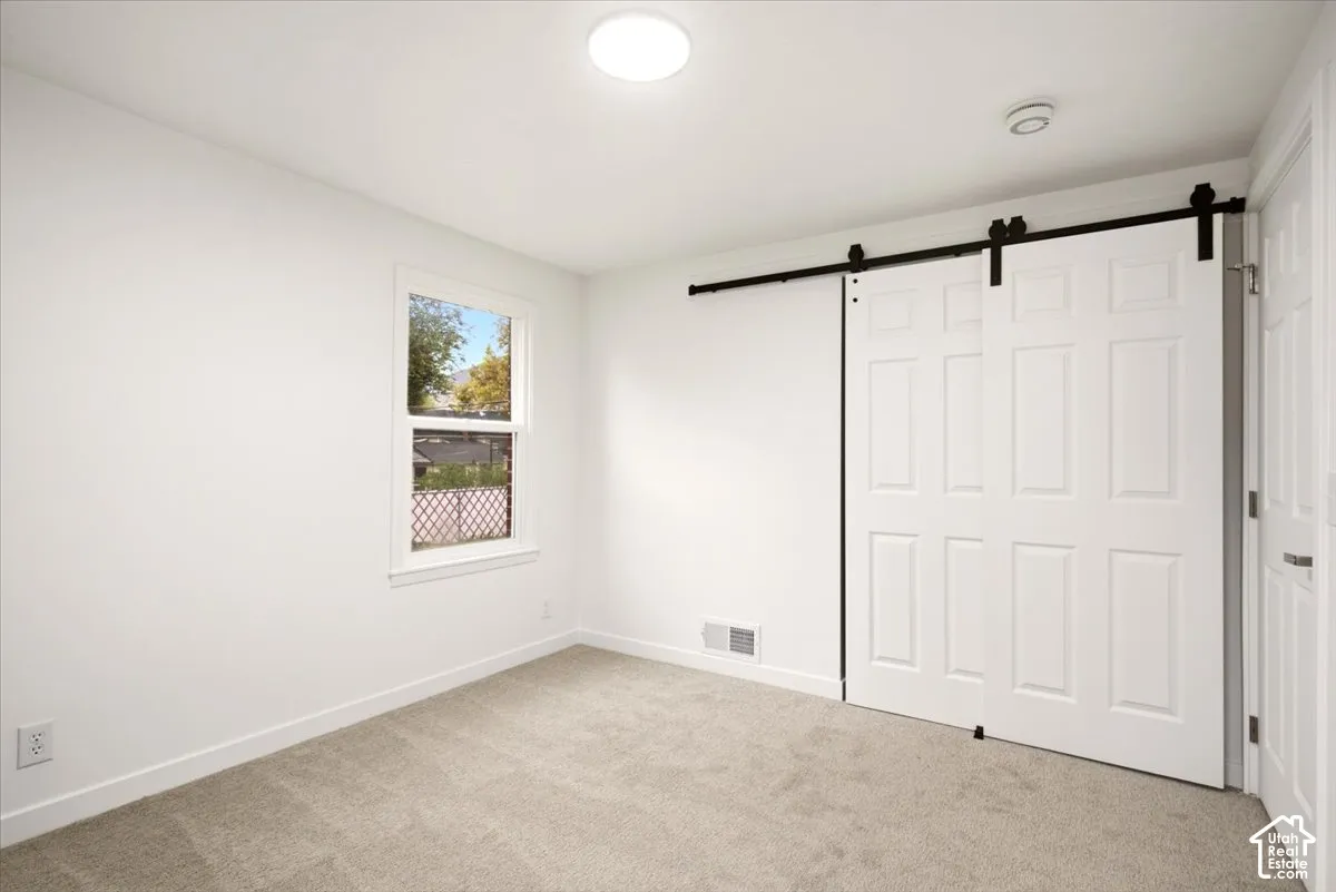 Neutral-toned carpeted flooring, sliding barn-style closet doors with matte black hardware, recessed ceiling lighting, and a single-hung window with a wood frame