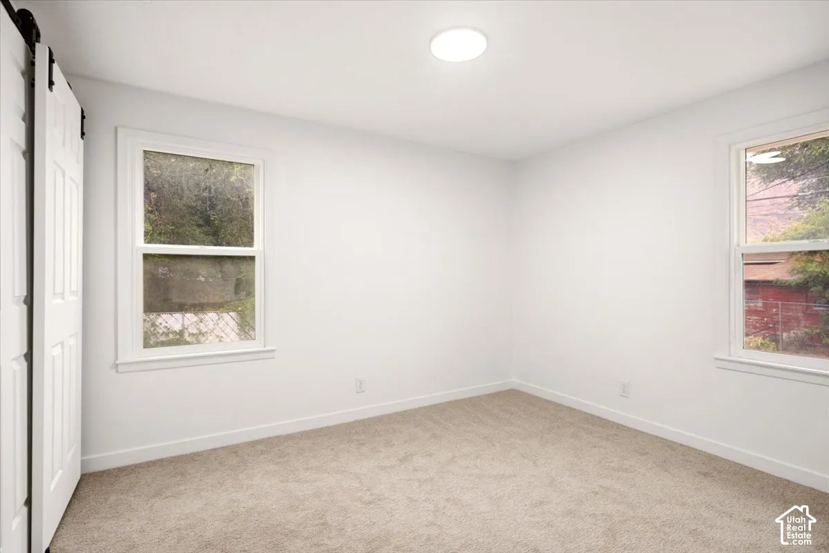 Neutral interior featuring carpeting, dual windows with white casing, and a white sliding barn-style door