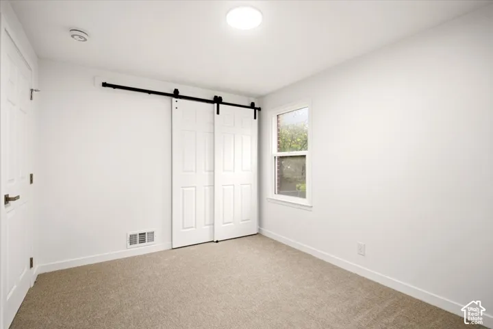 Room featuring wall-to-wall carpeting, dual white panel sliding barn doors with matte black hardware, and a single-hung window