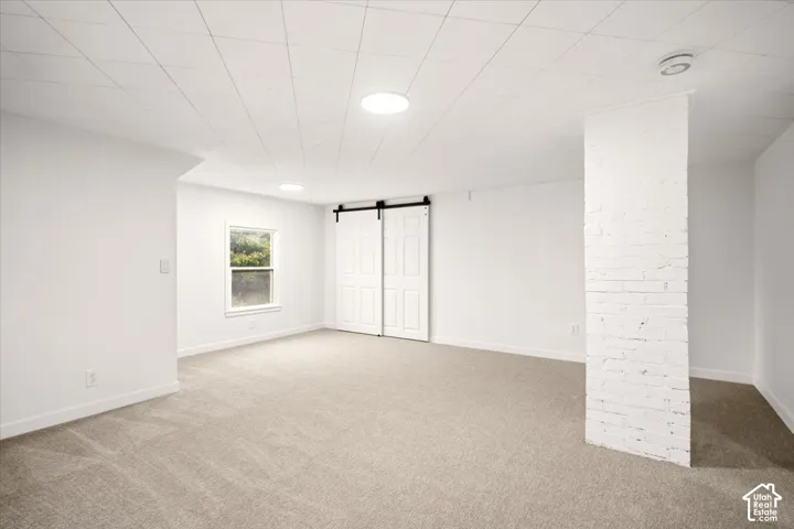 Open interior space featuring white painted brick architectural column, sliding barn-style doors, neutral carpeting, and recessed ceiling lighting