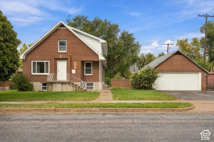 Brick exterior featuring a gabled roofline, concrete front stoop with decorative metal railing, and detached two-car garage