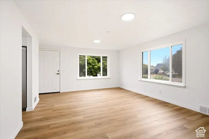 Open interior space featuring wood-finish flooring, two large windows with white trim, recessed lighting, and a solid-core entry door