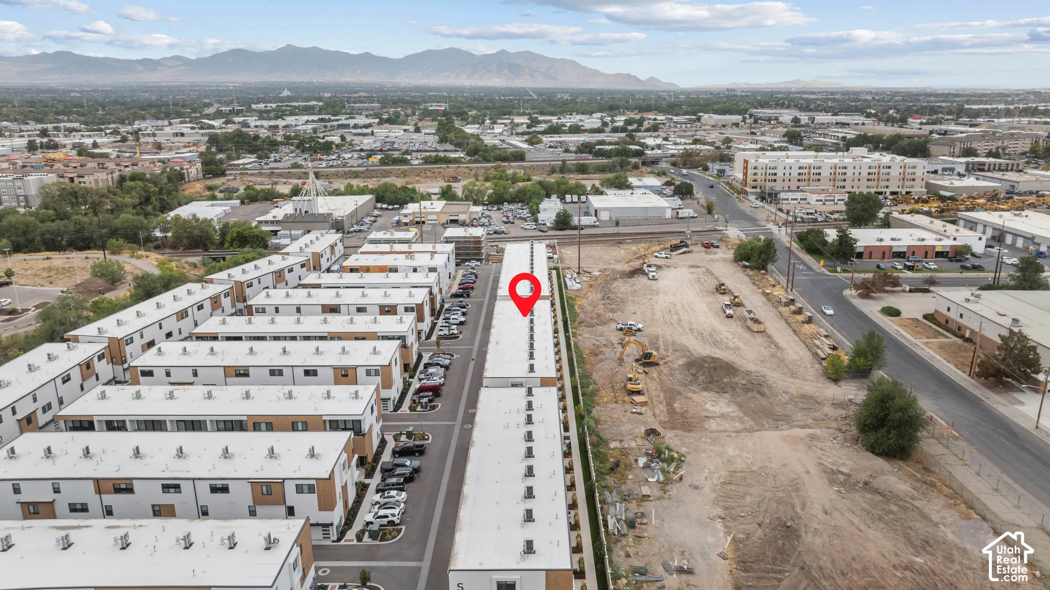 Aerial perspective of a multi-unit residential complex featuring flat roofs, modern siding, paved parking areas, and a mountain backdrop
