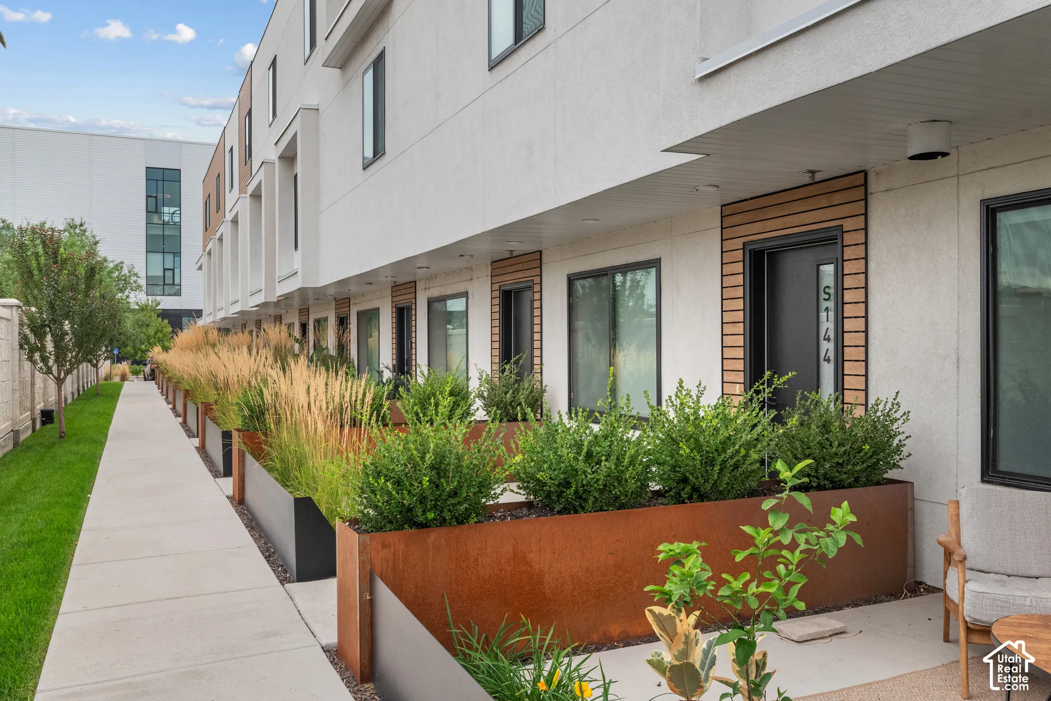 Modern multi-story exterior featuring light-toned smooth stucco, cedar plank accents, dark-framed windows, and integrated weathered-steel planter boxes
