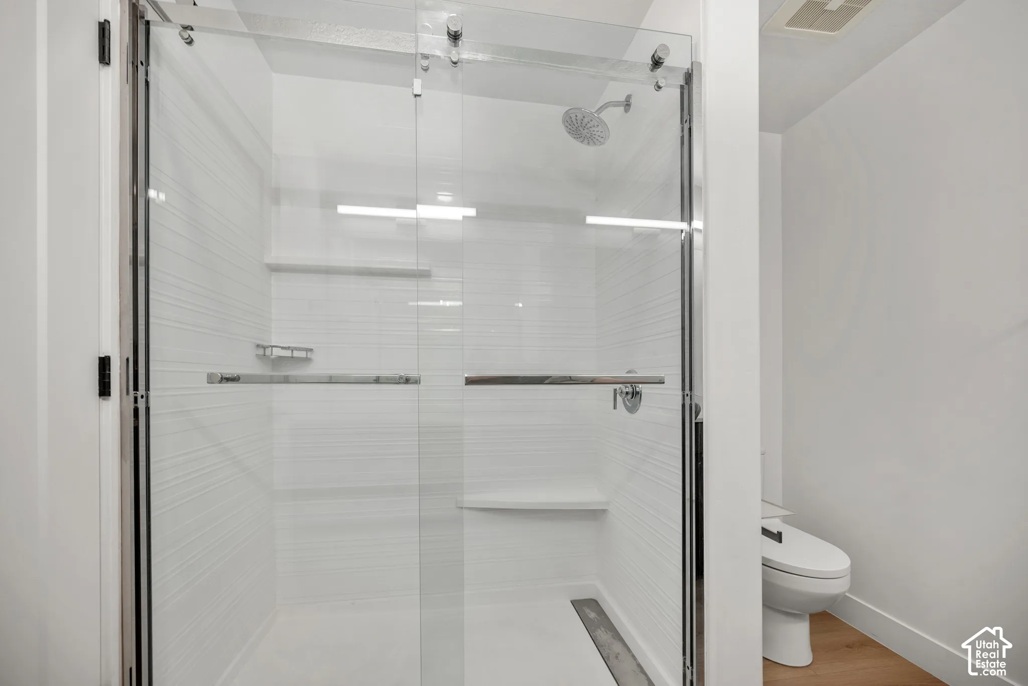 Walk-in shower featuring a sliding frameless glass door, textured horizontal tile surround, built-in shelving, chrome rainfall showerhead, and a fixed shower seat