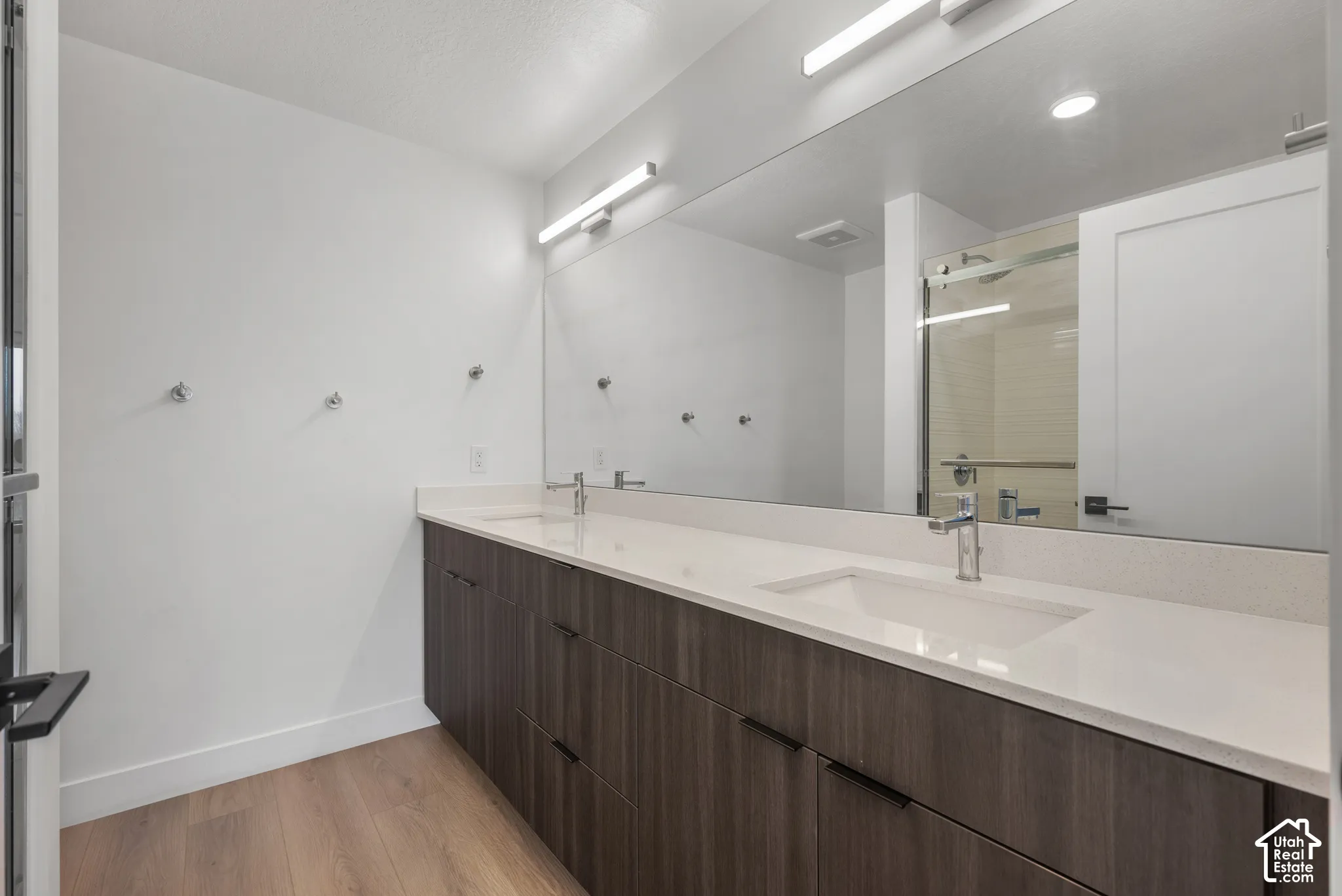 Dual-sink vanity featuring dark wood-finish cabinetry, quartz countertops, chrome fixtures, and a large-format vanity mirror with integrated lighting
