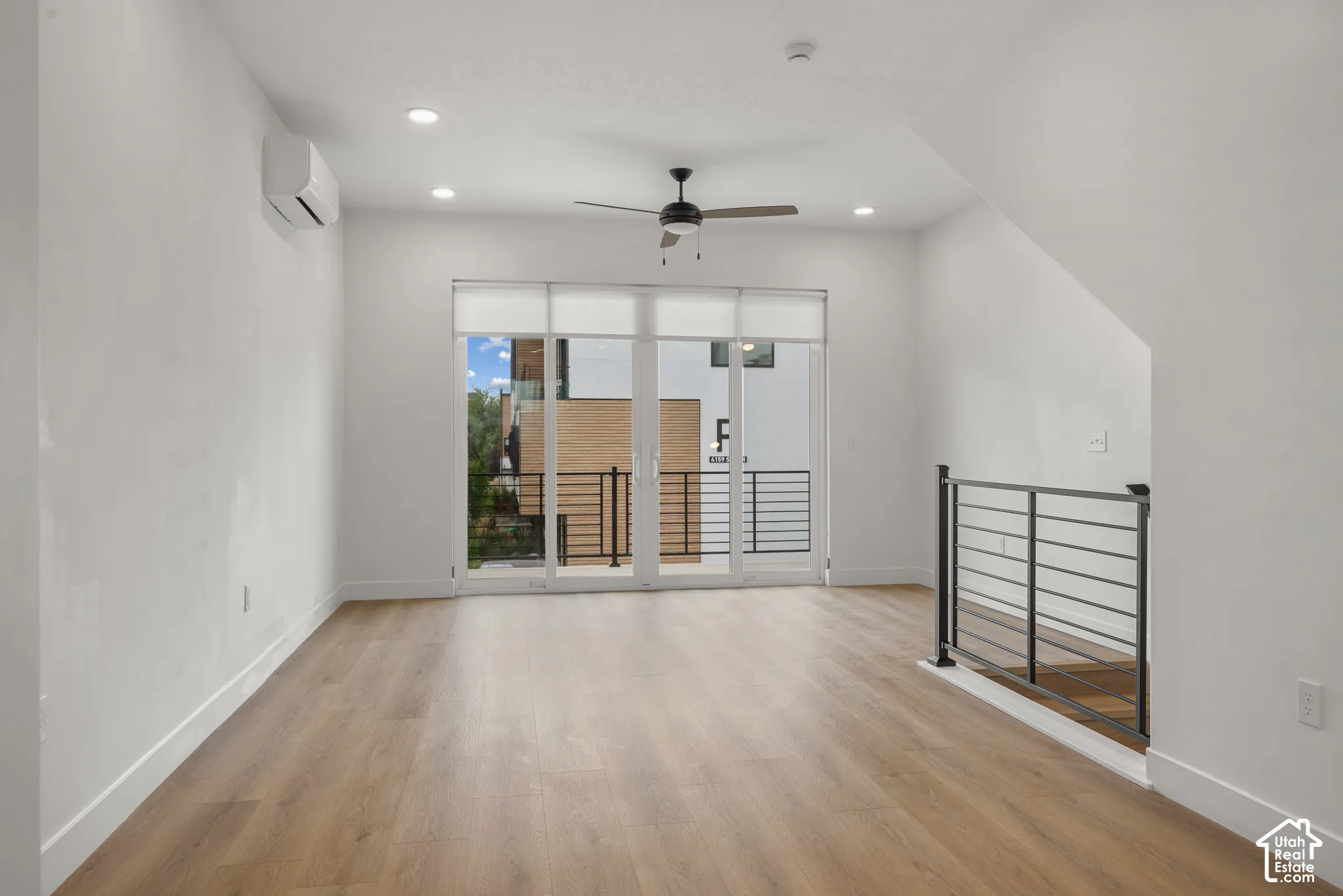 Interior space featuring wood-finish flooring, recessed lighting, a modern ceiling fan, a wall-mounted ductless climate control unit, and a metal horizontal-bar railing