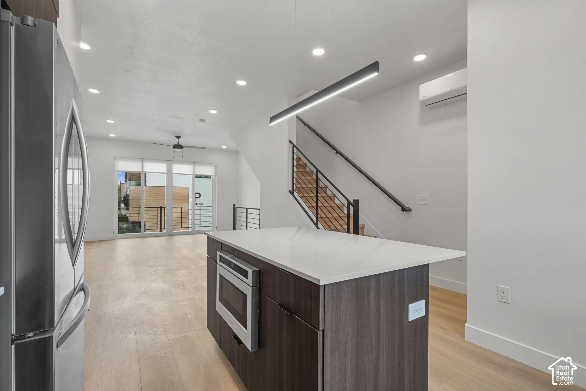 Kitchen featuring a central island with a solid surface countertop and built-in microwave, wood-finish flooring, recessed lighting, linear pendant lighting, and a staircase with a black metal railing