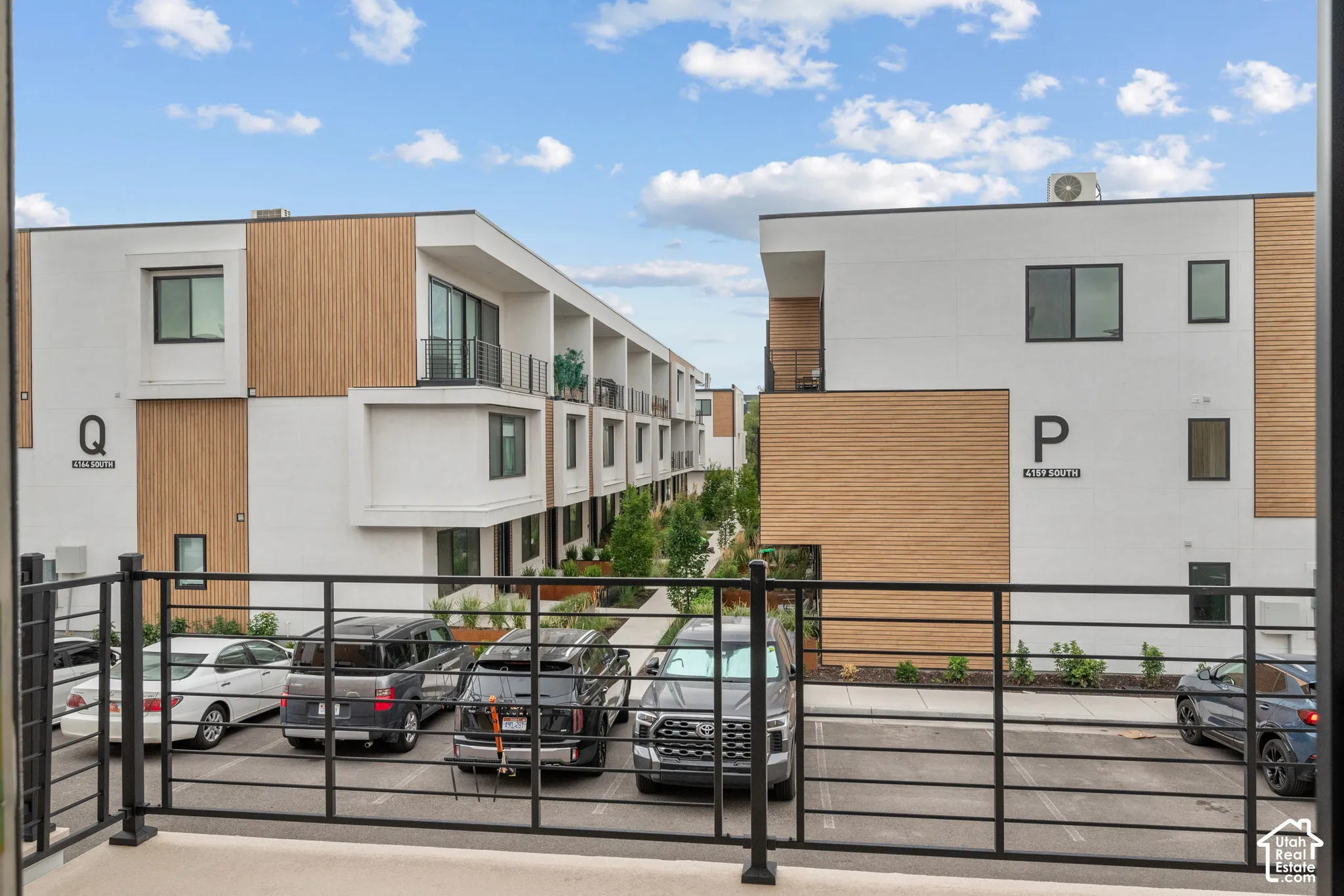 Modern architectural exterior featuring smooth-finish stucco and wood-tone cladding, private metal-railing balcony, and paved parking area