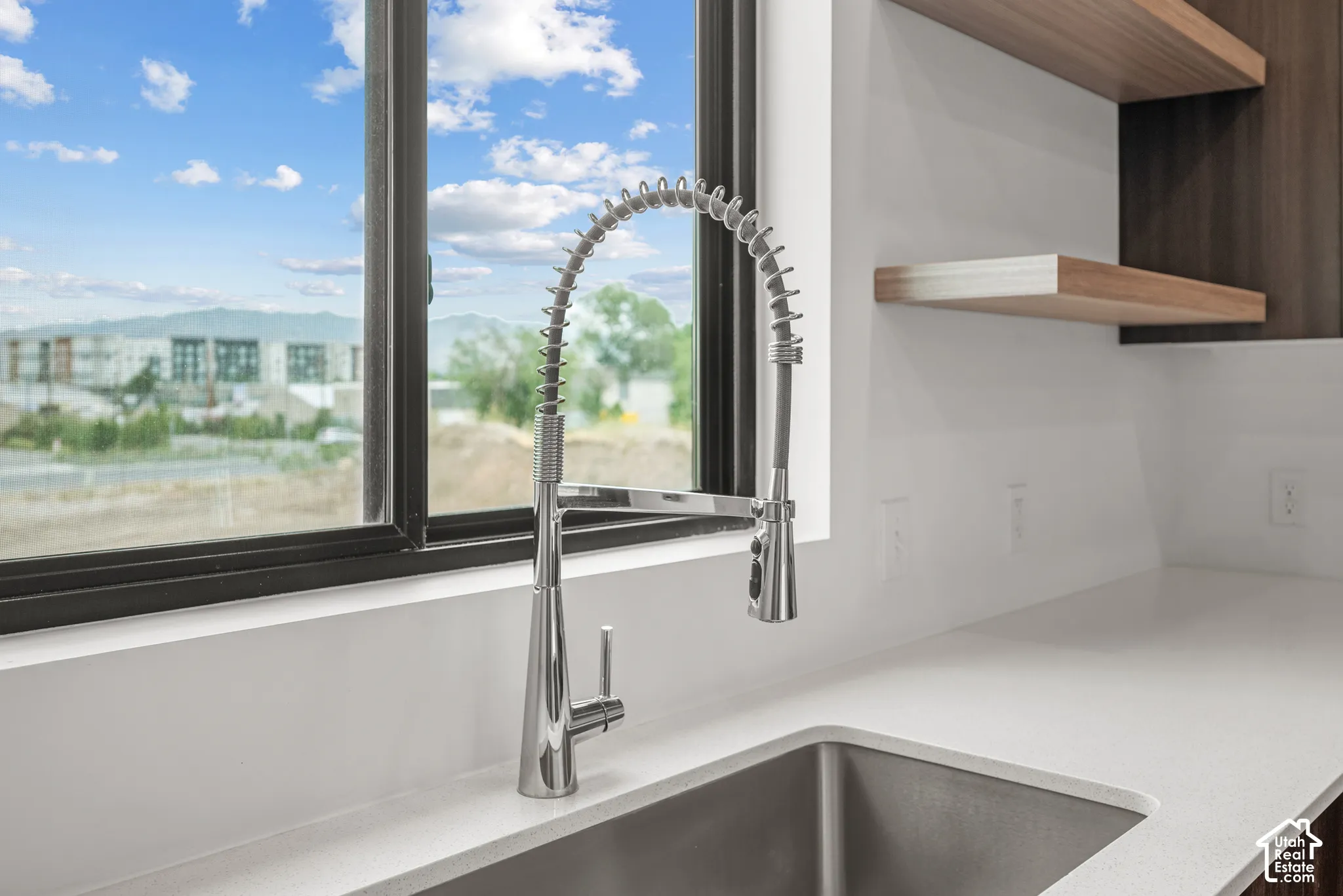 Stainless steel industrial-style pull-down faucet, undermount sink, solid surface countertop, and floating wood-finish shelving