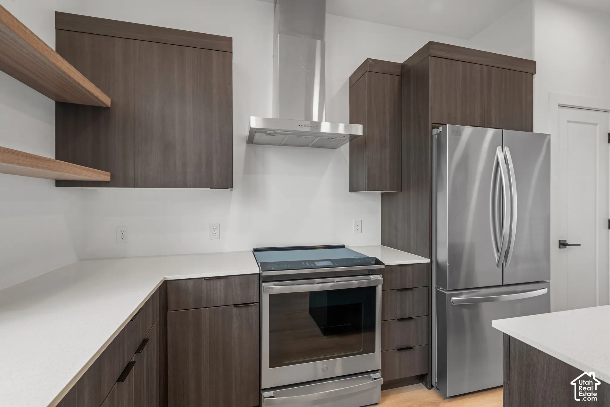 Kitchen featuring flat-panel cabinetry, open shelving, stainless steel appliances, a chimney-style range hood, and quartz countertops