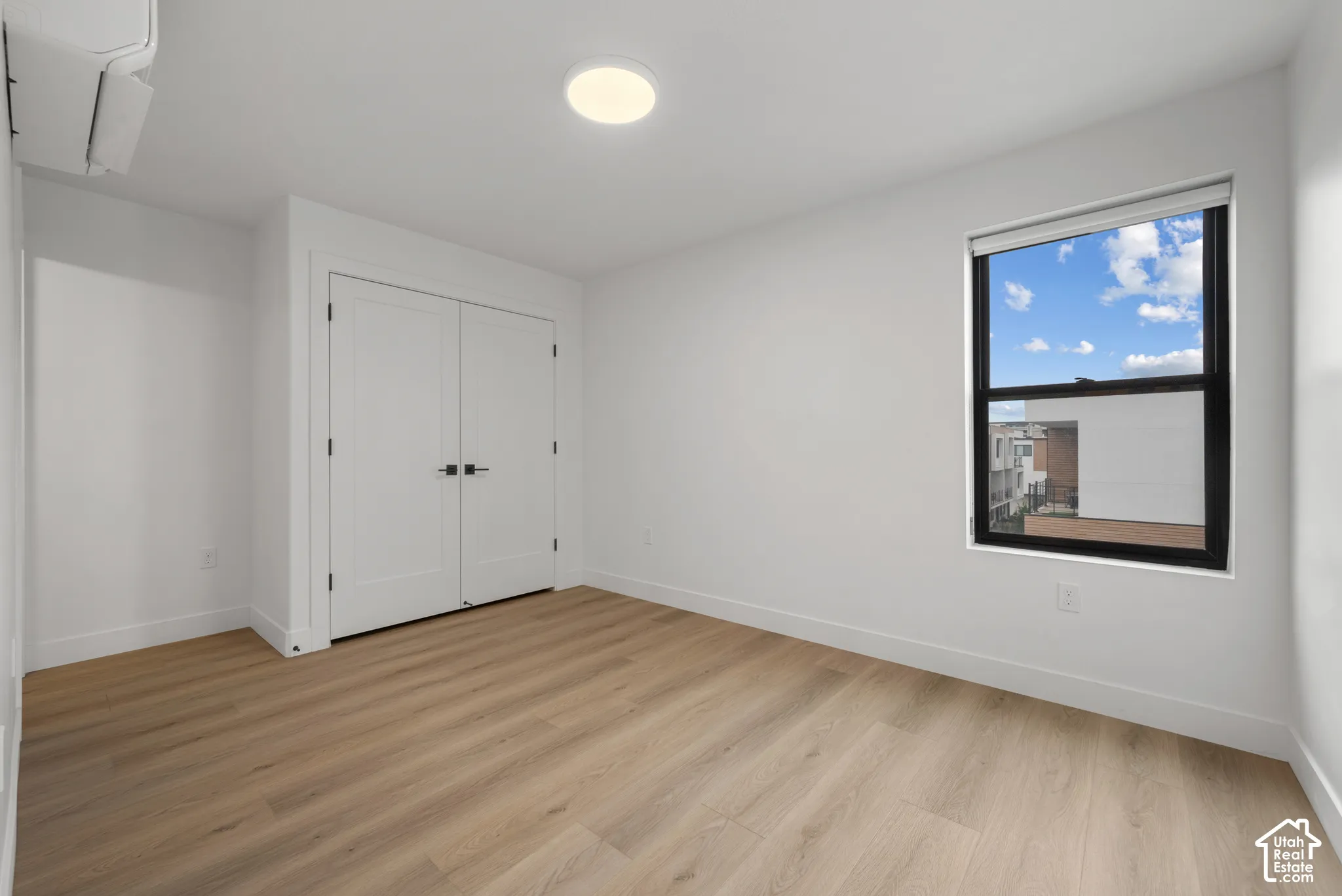 Interior space featuring light wood-finish flooring, double-door closet with matte black hardware, flush-mount circular lighting, and a window with black framing