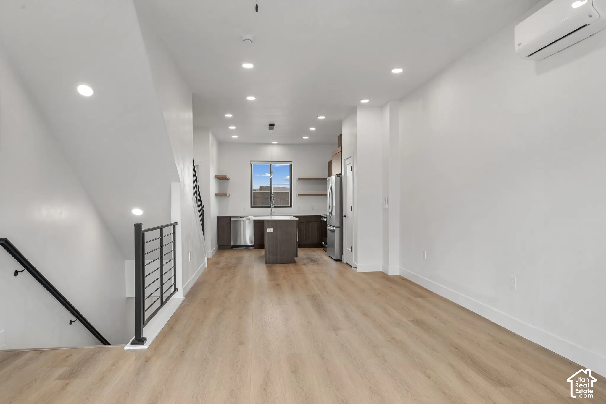 Open-concept area featuring wood-finish flooring, recessed lighting, a kitchen island with stone-surface countertop, custom cabinetry, and staircase with metal railing