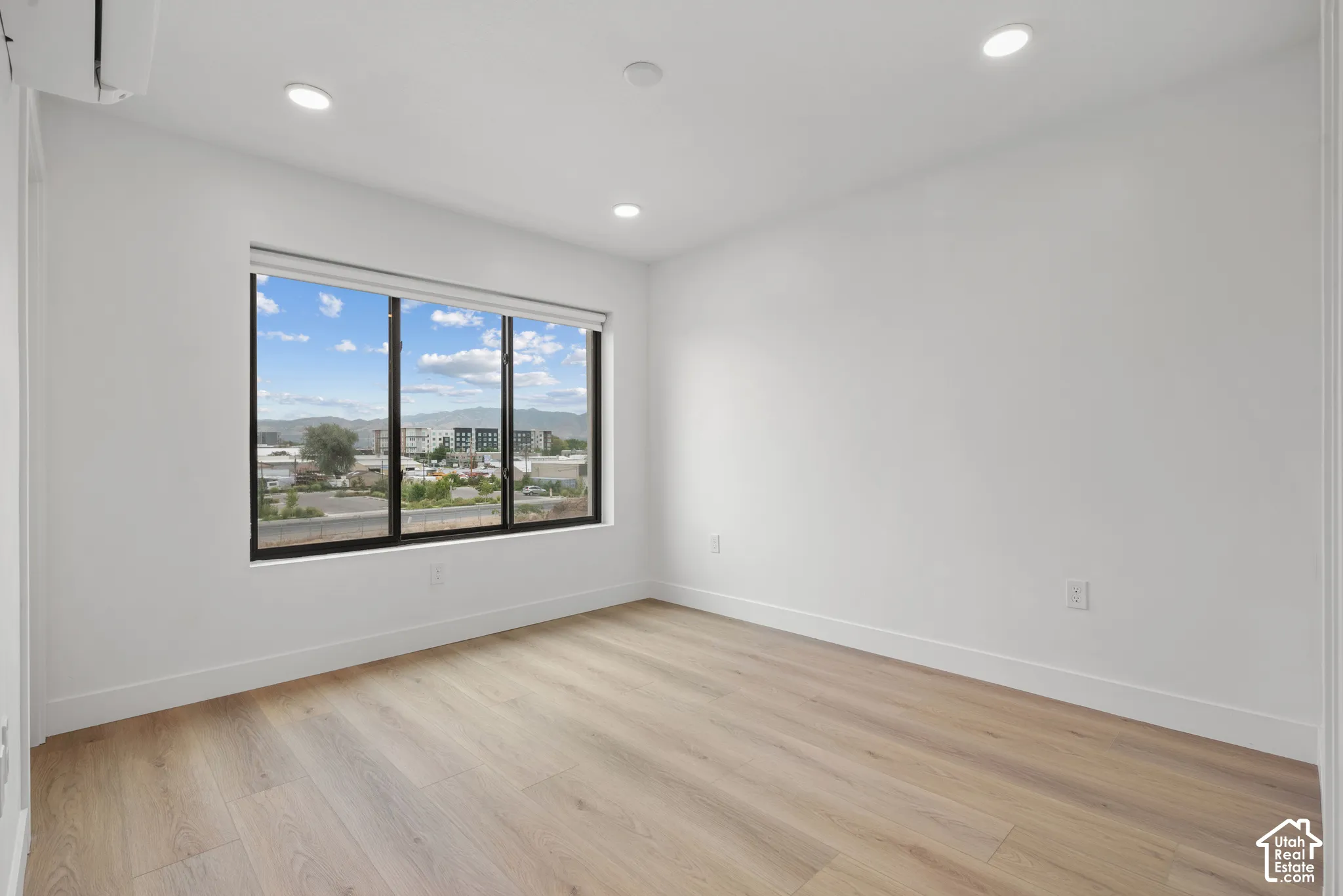 Interior space featuring wood-finish flooring, recessed lighting, a wall-mounted climate control unit, and a large window with exterior mountain scenery