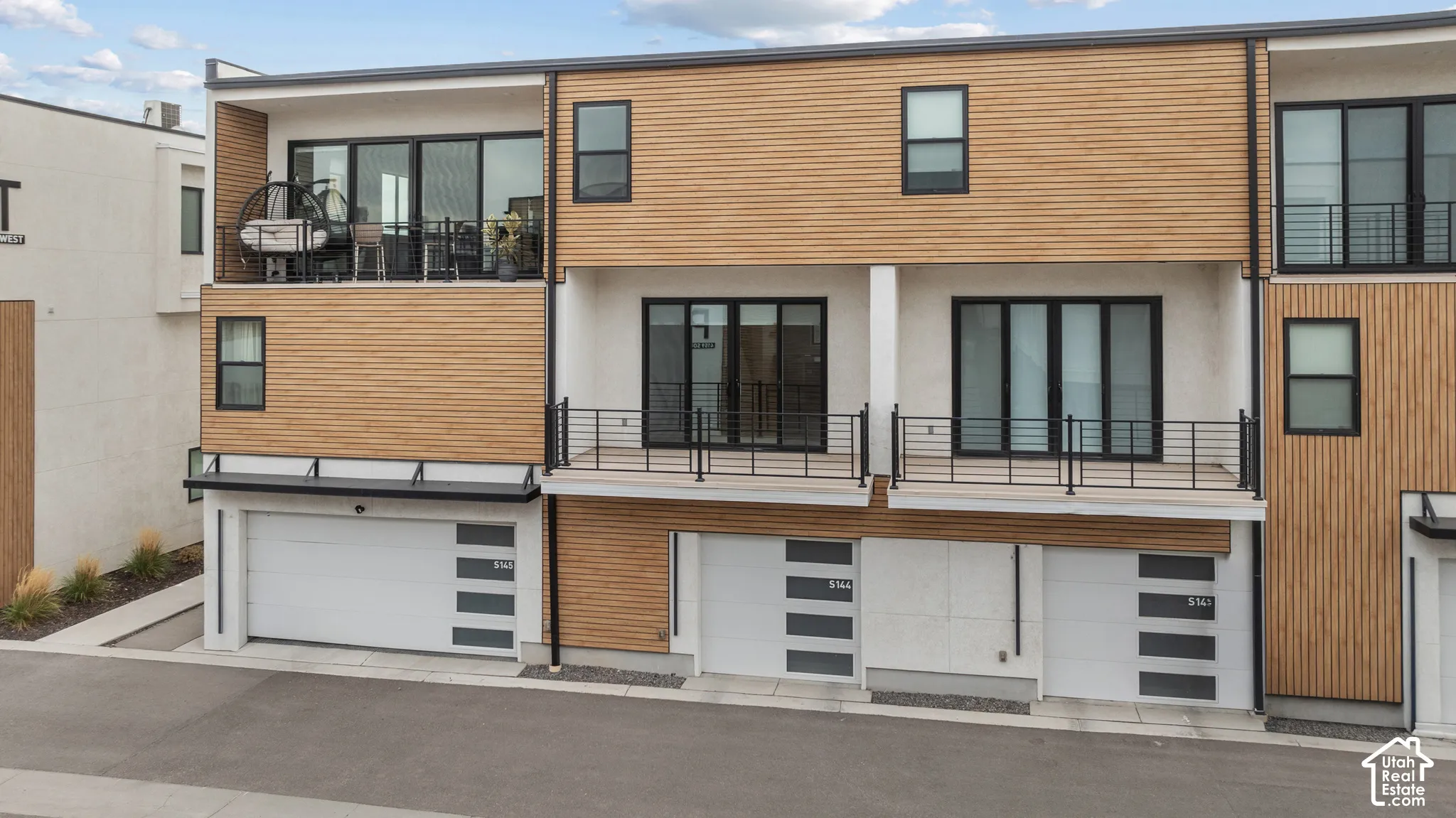 Contemporary multi-level exterior featuring horizontal wood-slat siding, smooth stucco finishes, tiered balconies with black metal railings, and multi-panel sectional garage doors