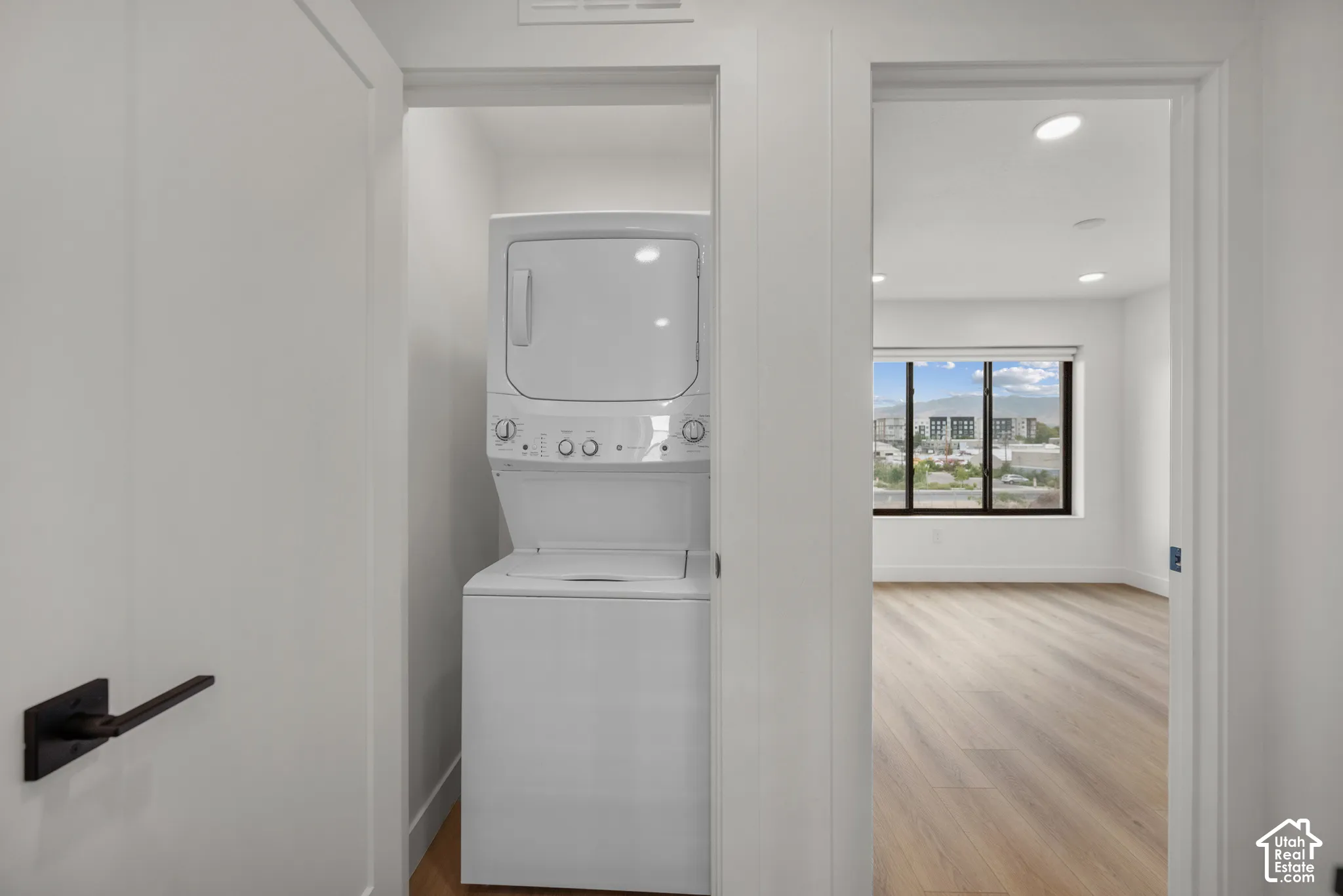 Stacked laundry unit, wood-finish flooring, recessed lighting, and black hardware