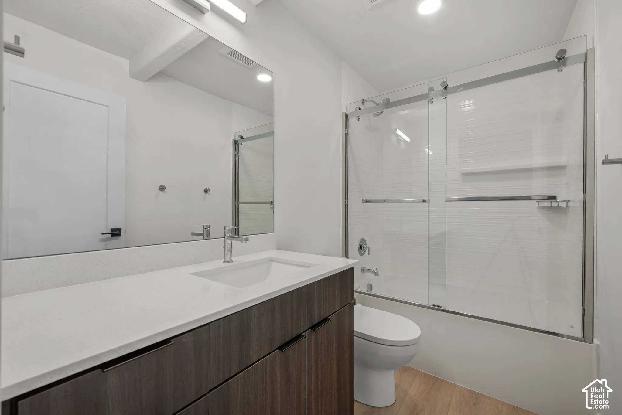 Wood-finish cabinetry with a solid-surface countertop, rectangular integrated sink, chrome faucet, and floor-to-ceiling glass-enclosed shower with horizontal tile surround